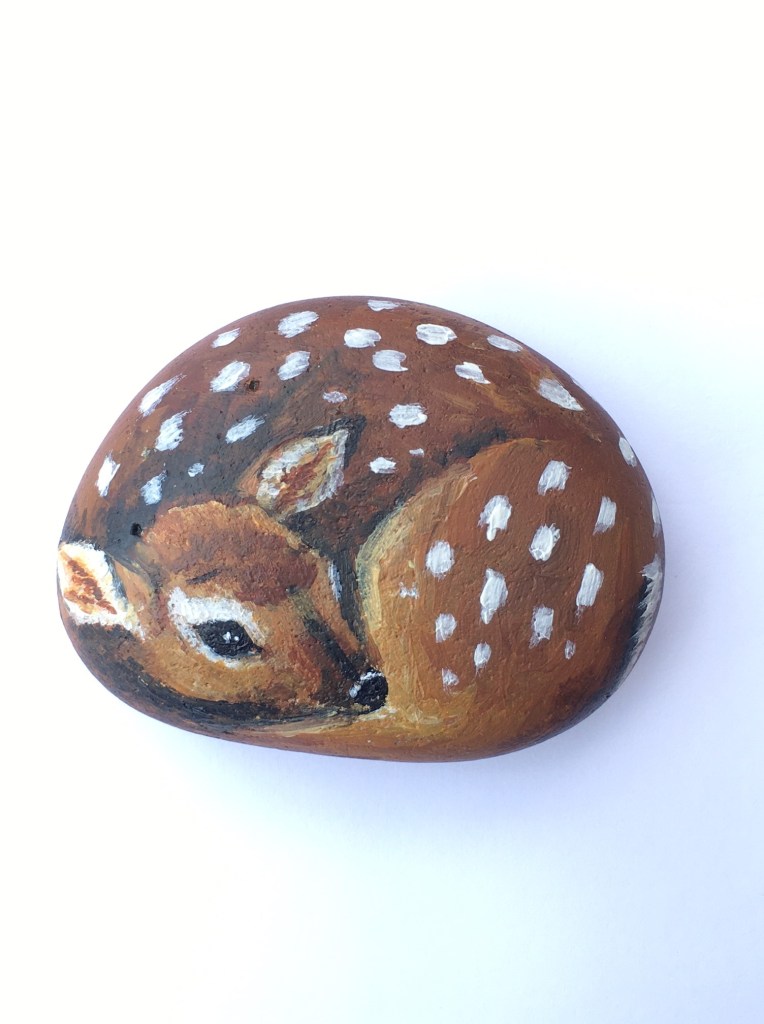 Fawn rock painting baby deer curled up.